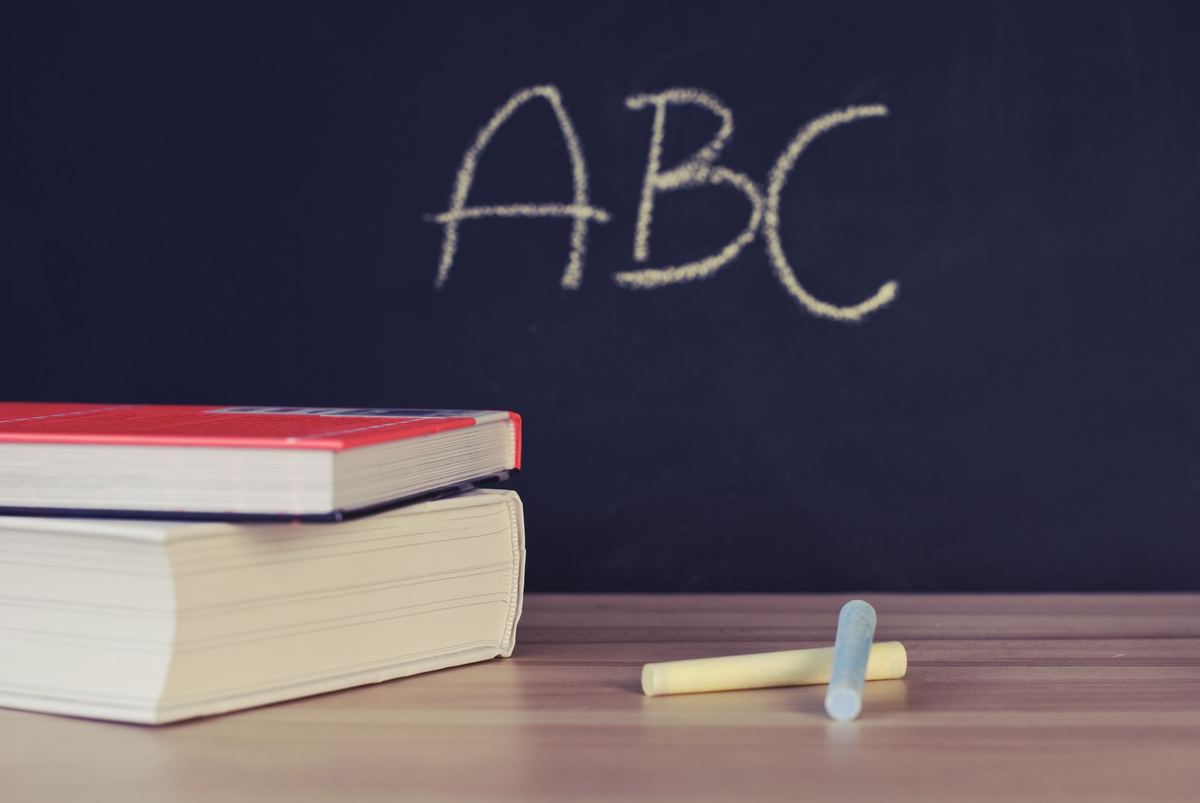 Chalk sticks and stacked books in front of a blackboard with ABC written on it.