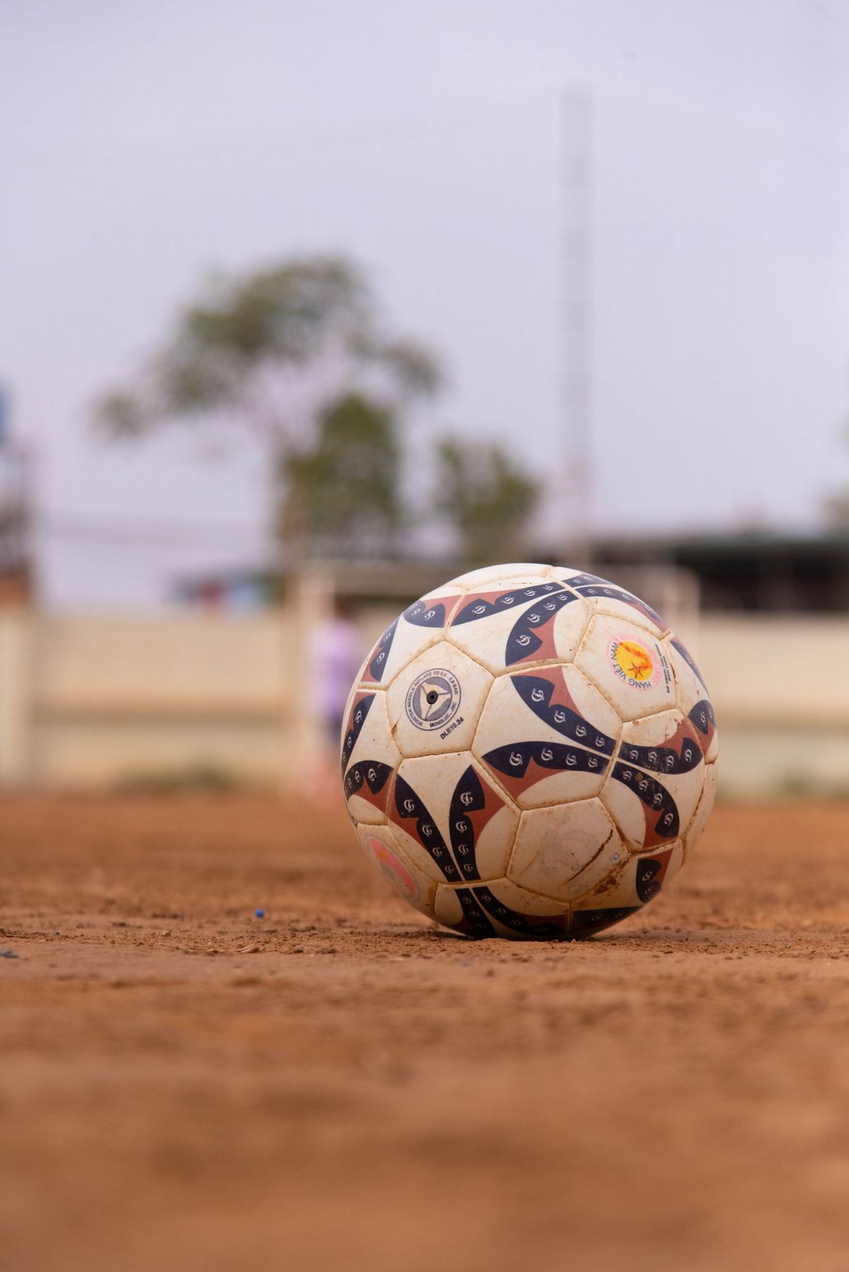 A well-worn football rests on red earth in warm afternoon light.