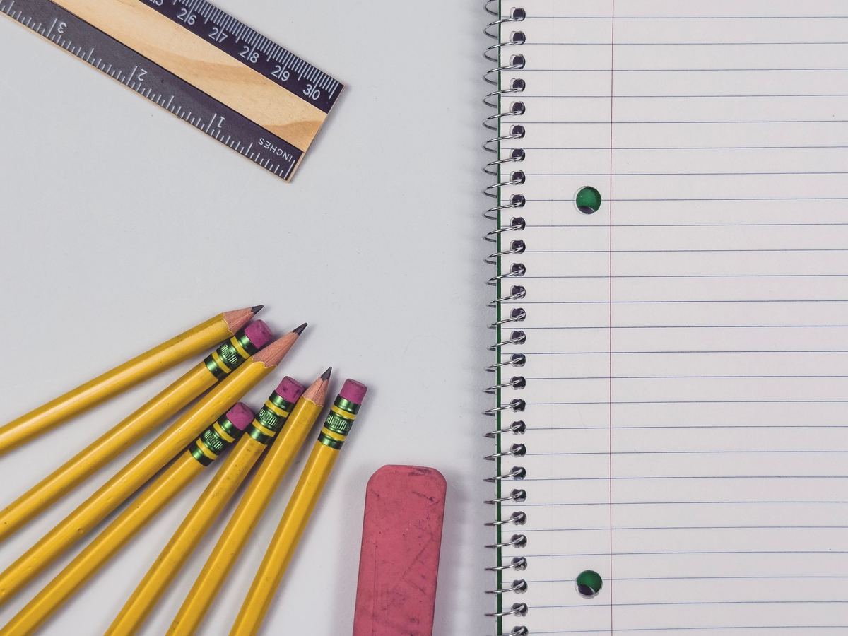 Yellow pencils, a pink eraser, a wooden ruler and a ruled notebook laid out neatly on a desk.